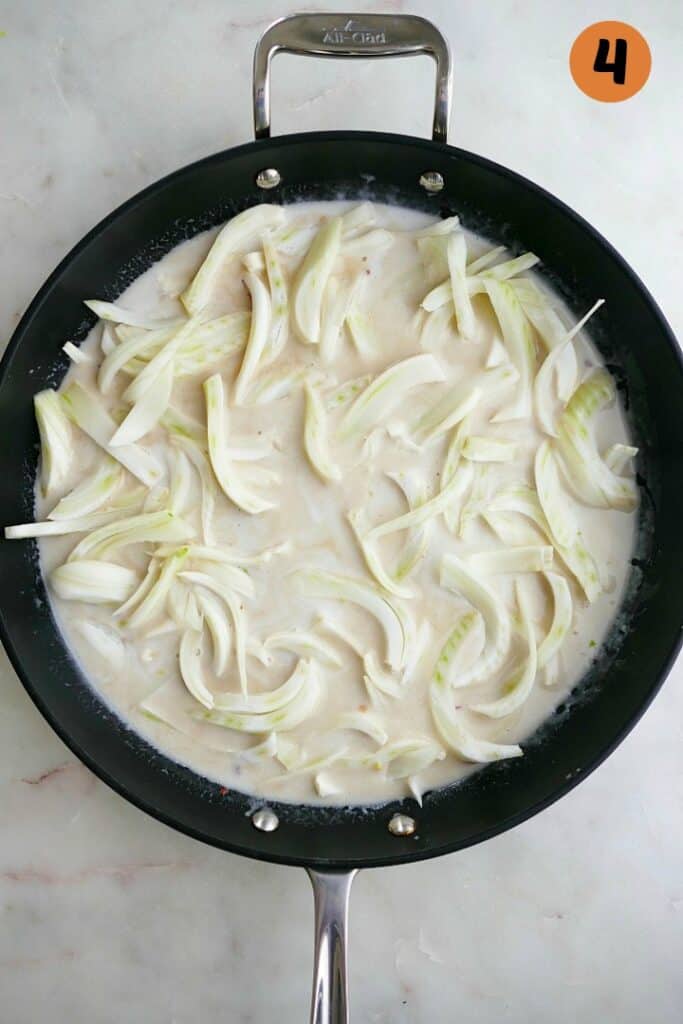 fennel cooking in coconut milk in a black skillet on a white counter