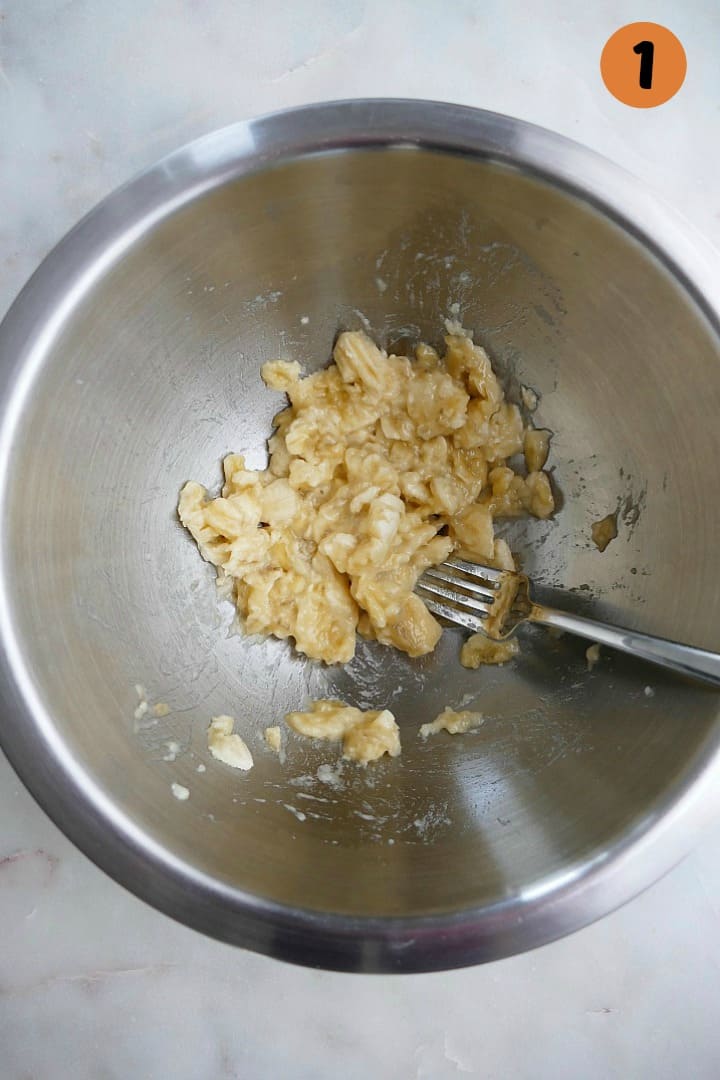 mashed bananas in a silver mixing bowl with a fork on a white counter