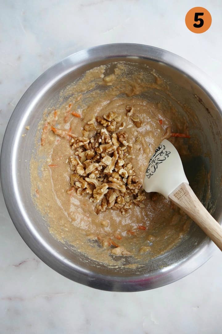 carrot bread batter with chopped walnuts folded into it in a silver mixing bowl