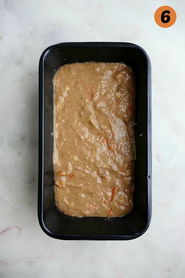 carrot bread batter spread out in a greased loaf pan on a white counter