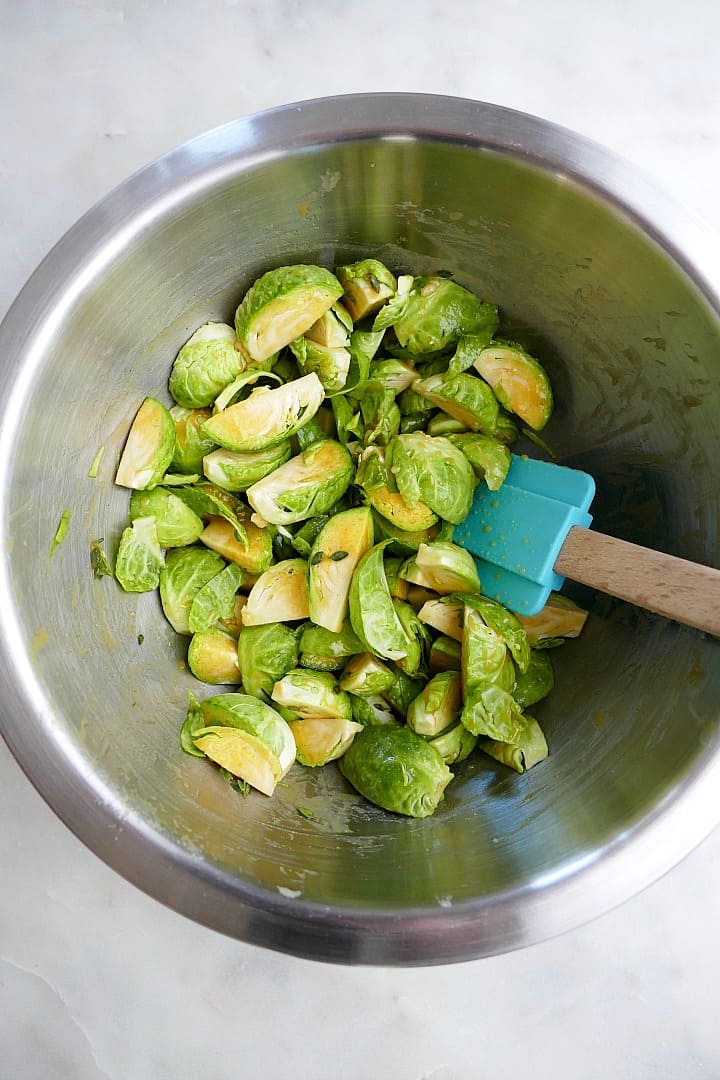 sliced brussels sprouts in a metal mixing bowl with a blue spatula