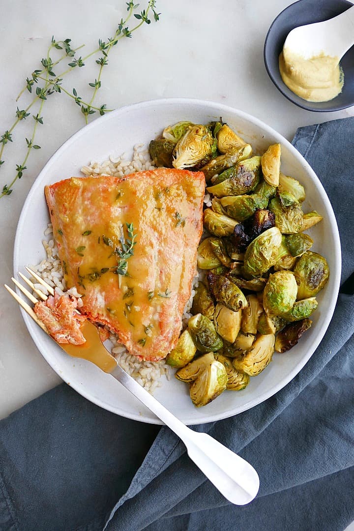 maple mustard salmon and brussels sprouts on a white plate with a gold fork