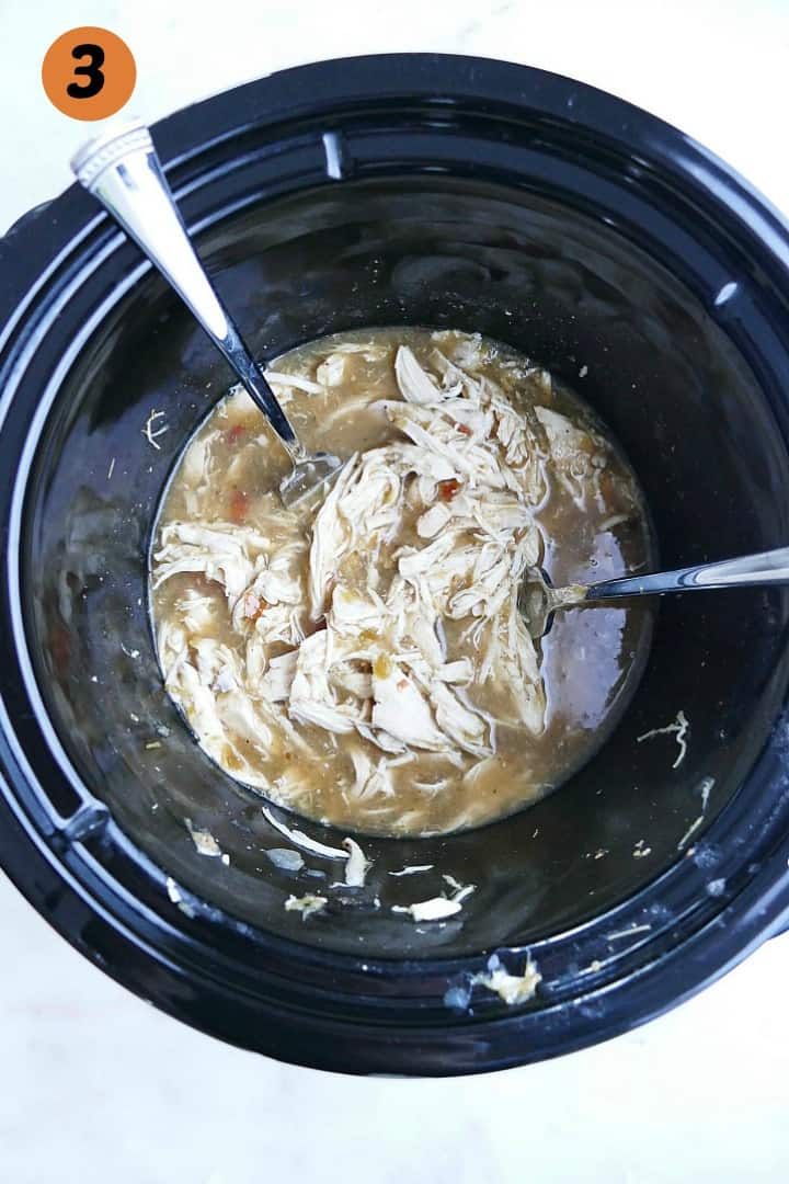 shredded mexican chicken in a slow cooker on a white counter with two forks