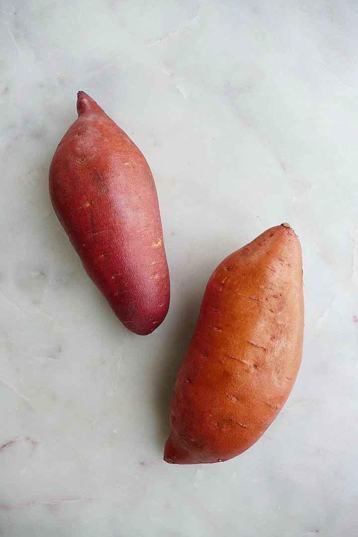 two large sweet potatoes on a white marble counter top