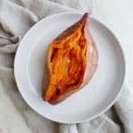 a cooked sweet potato sliced open on a white plate on top of a gray napkin