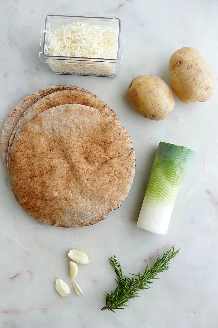 ingredients for potato leek pizza with rosemary and gruyere on a white counter