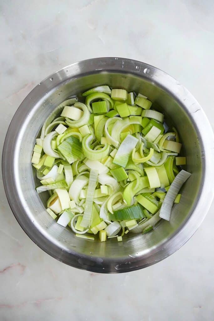 chopped leeks in a metal bowl of water on a white counter