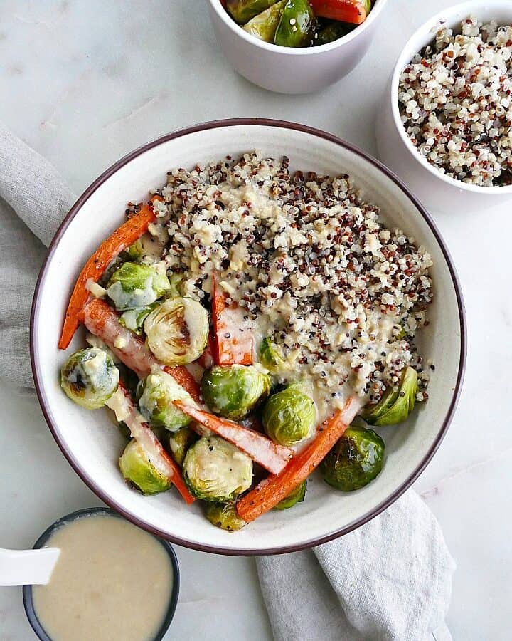 roasted vegetables with tri-colored quinoa and maple ginger tahini in a white bowl