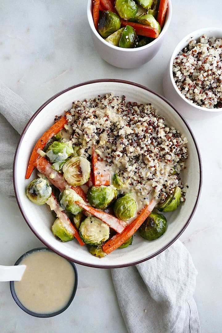 roasted vegetables with tri-colored quinoa and maple ginger tahini in a white bowl on a counter