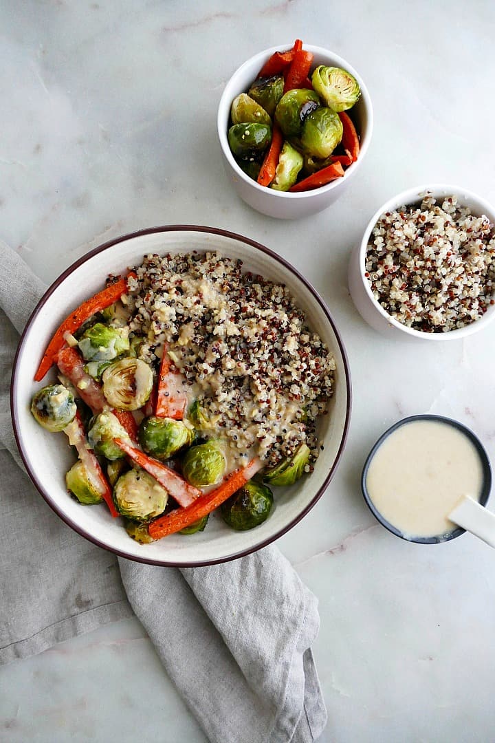 quinoa with vegetables in a white bowl next to small bowls of ingredients on a counter