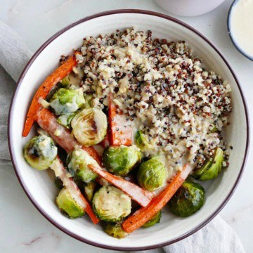 quinoa with roasted carrots and brussels sprouts in a white bowl on a gray napkin