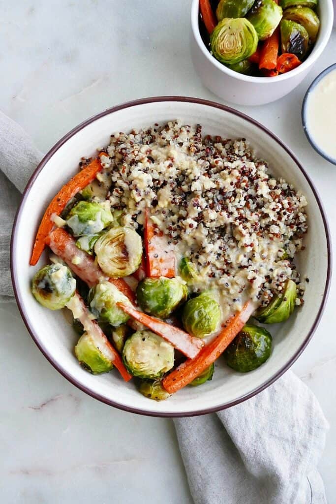 quinoa with roasted carrots and brussels sprouts in a white bowl on a gray napkin