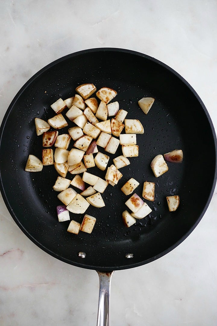 diced turnips and olive oil cooking in a black skillet on a white counter