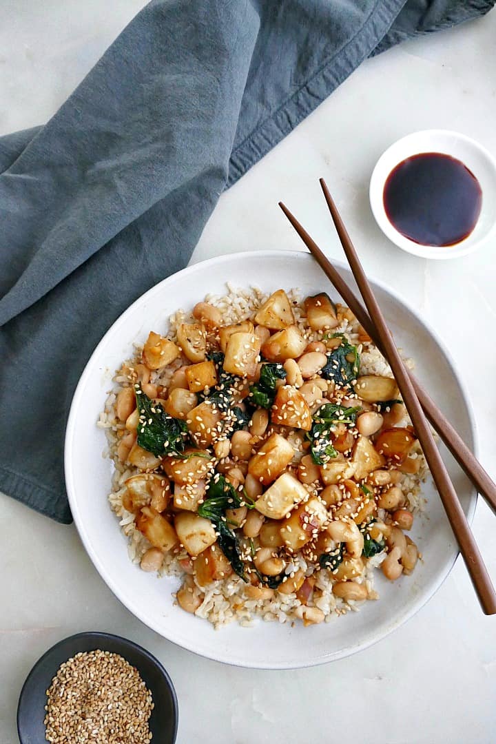 turnip stir fry on a white plate with brown chopsticks balanced on the side