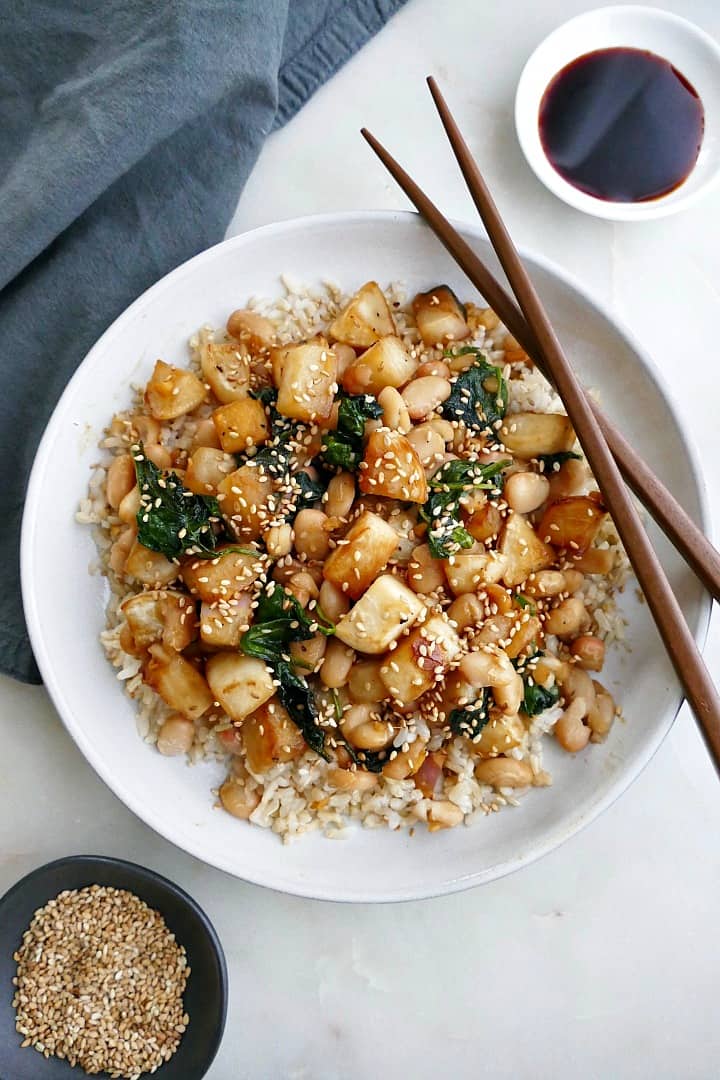 turnip stir fry on a white plate with brown chopsticks next to a blue napkin