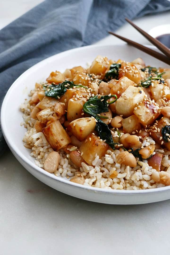 side view of turnip stir fry on a white plate with a blue napkin in back