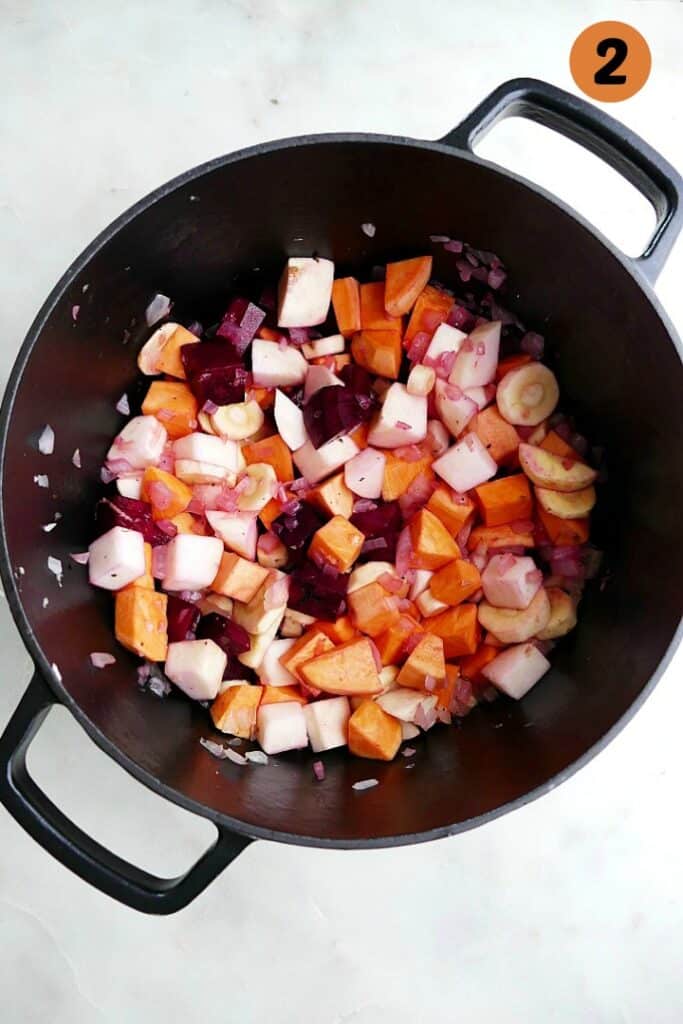 diced veggies cooking in a cast iron dutch oven on a counter