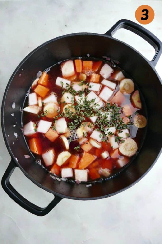 diced veggies with broth and herbs in a cast iron dutch oven on a counter