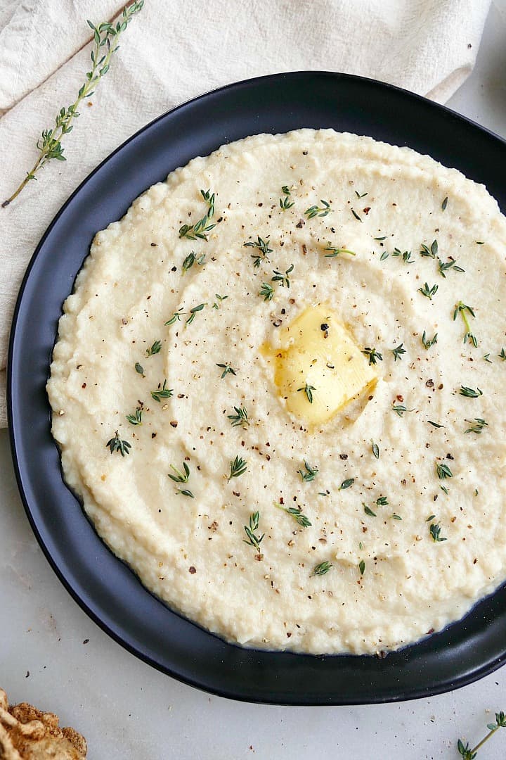 close up of celery root mash with pat of butter and thyme on a black plate