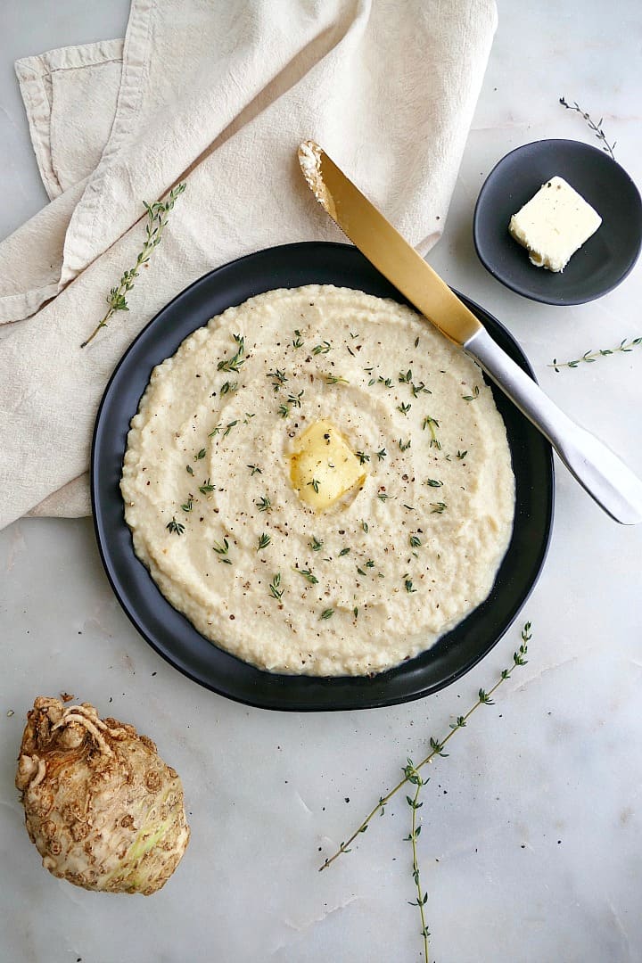 mashed celeriac with thyme and butter on a black plate with gold knife