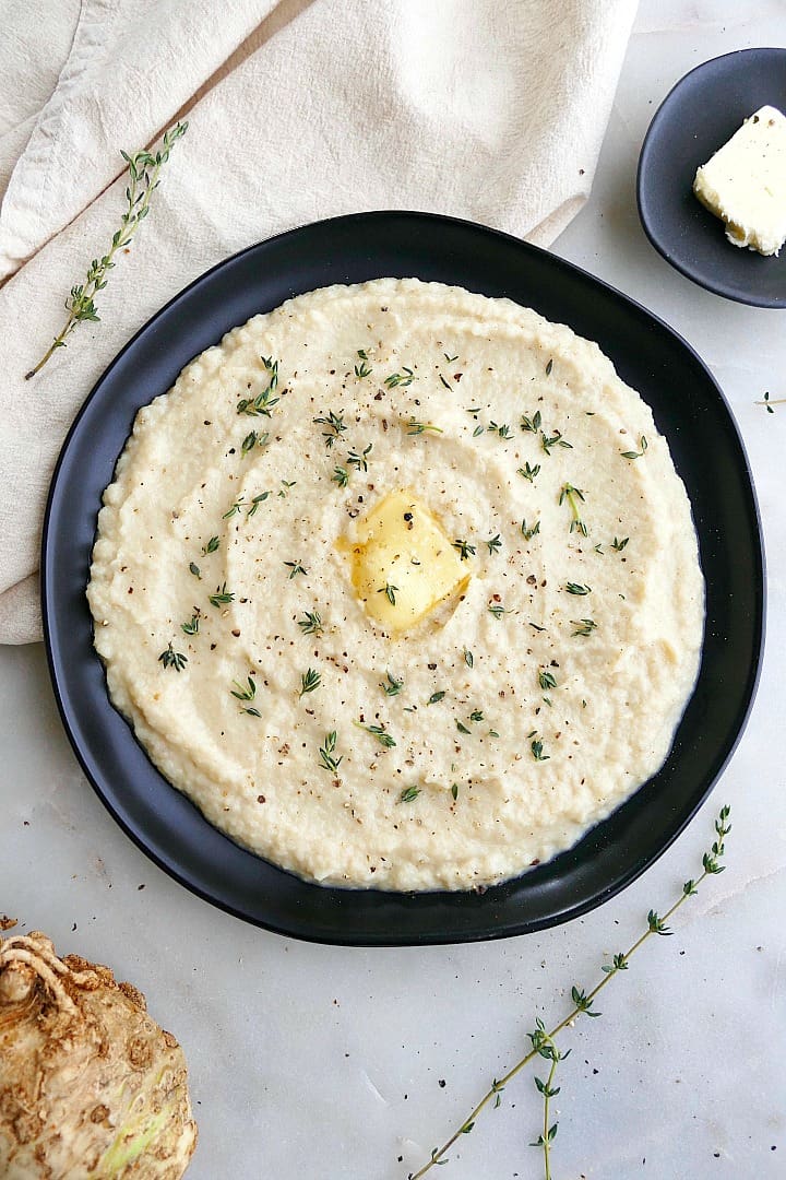 celeriac mash with a pat of butter and thyme leaves on a black plate