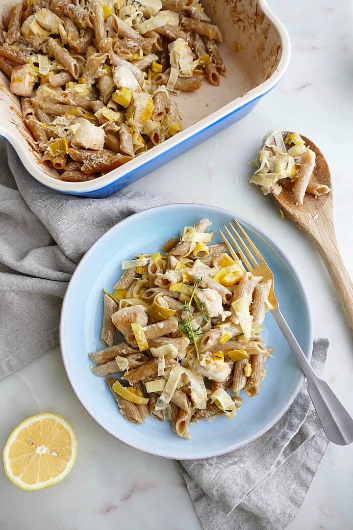 blue plate with chicken and leek pasta bake next to a blue serving dish