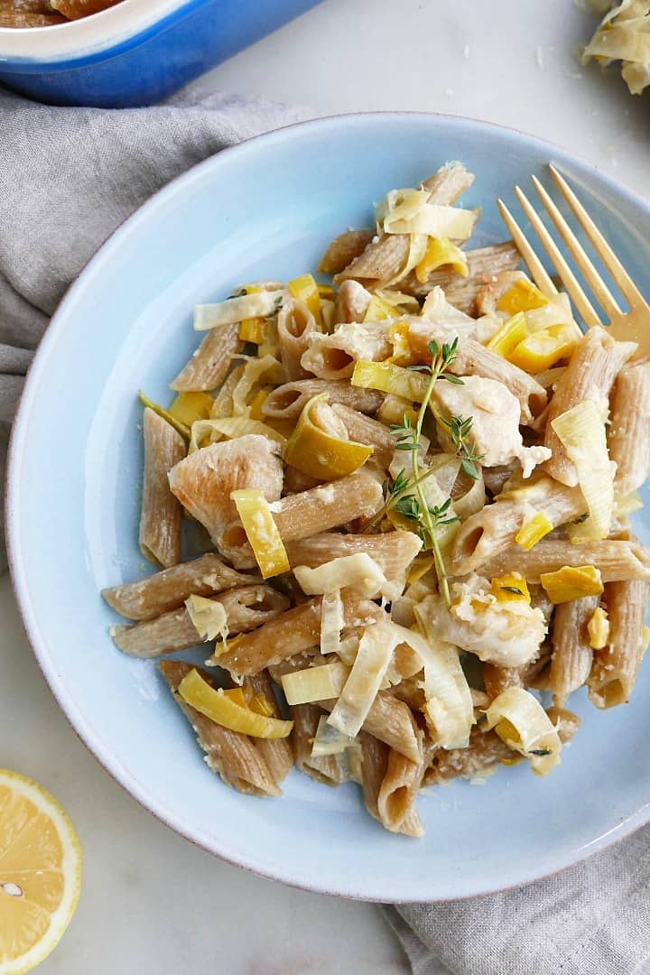 Close up of chicken and leek pasta bake on a blue plate with a gold fork. 