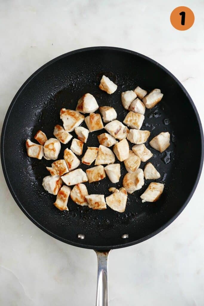 diced chicken cooking in a black skillet on a white counter with 1 in the corner