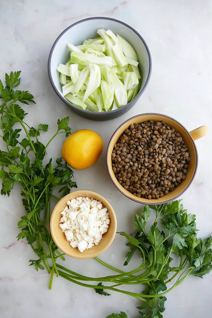 parsley, feta, lemon, lentils, and fennel in bowls on a counter