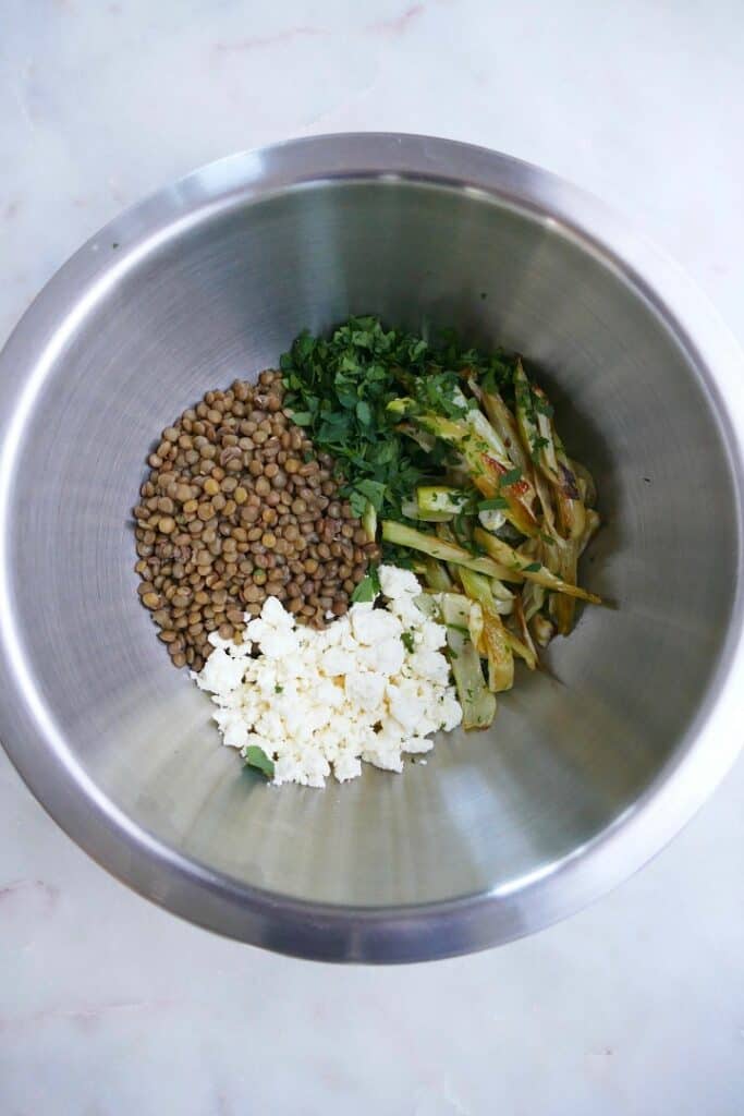 lentils, feta, fennel, and parsley in a silver mixing bowl on a counter