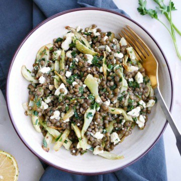 a white bowl with fennel and lentil salad on top of a blue napkin