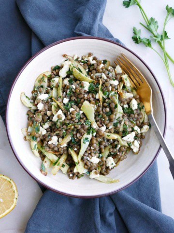 a white bowl with fennel and lentil salad on top of a blue napkin