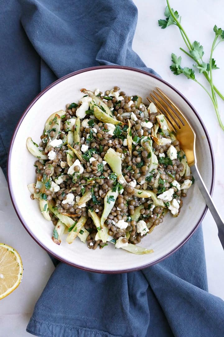 a white bowl with fennel and lentil salad on top of a blue napkin