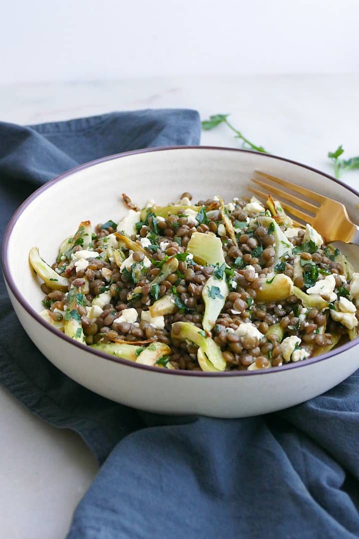 side view of a white bowl with fennel lentil salad on a blue napkin