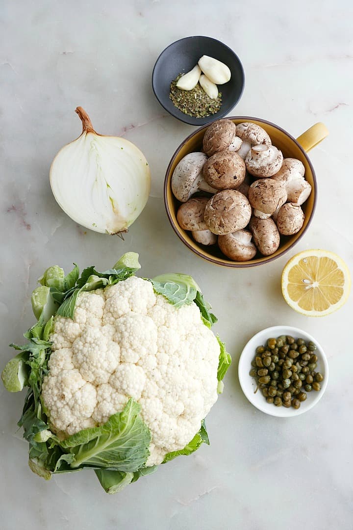 cauliflower, mushrooms, onion, lemon, capers, garlic, and oregano on a white counter
