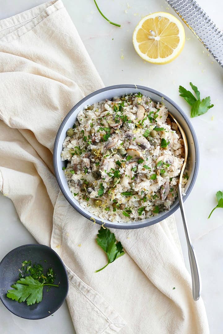 greek cauliflower rice in a blue and white bowl with a gold spoon on a counter