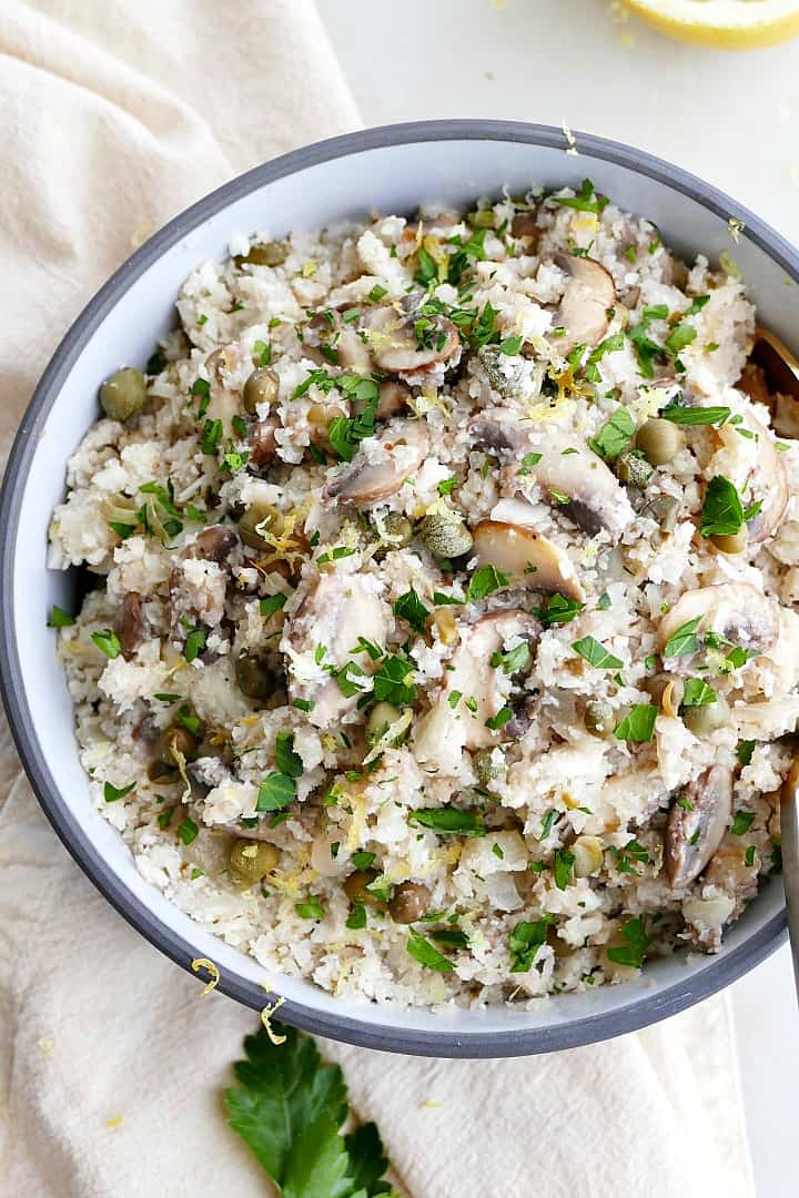 close up of greek cauliflower rice in a gray bowl with mushrooms and chopped parsley