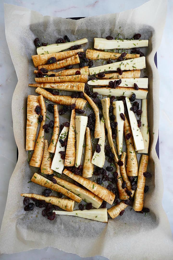 sliced parsnips, rosemary, and raisins on a baking sheet lined with parchment paper