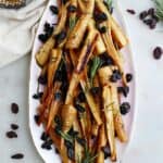 honey roasted parsnips and raisins on a pink oval tray on a white counter