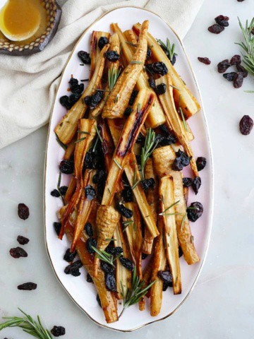 honey roasted parsnips and raisins on a pink oval tray on a white counter