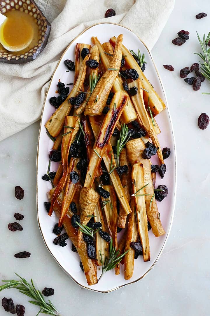 honey roasted parsnips and raisins on a pink oval tray on a white counter