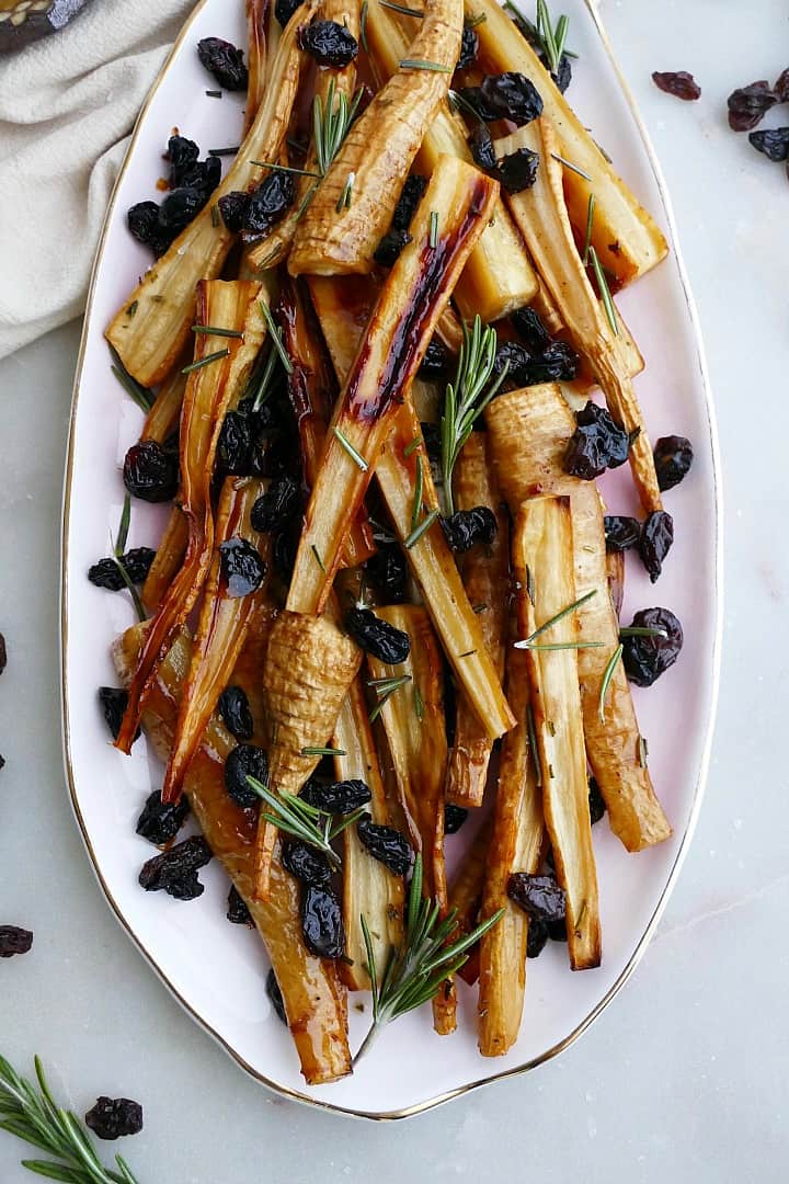 honey roast parsnips and raisins on a pink oval tray on a counter