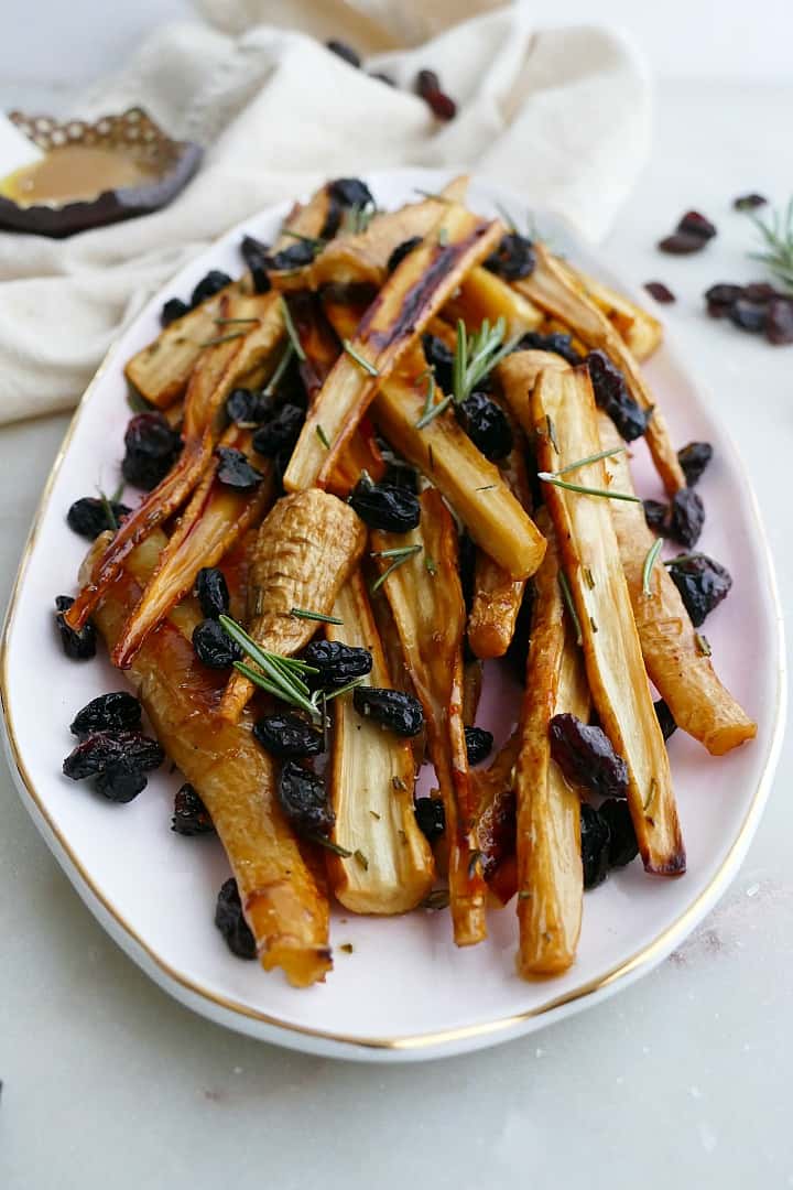 close up of honey roast parsnips and raisins on a pink oval tray