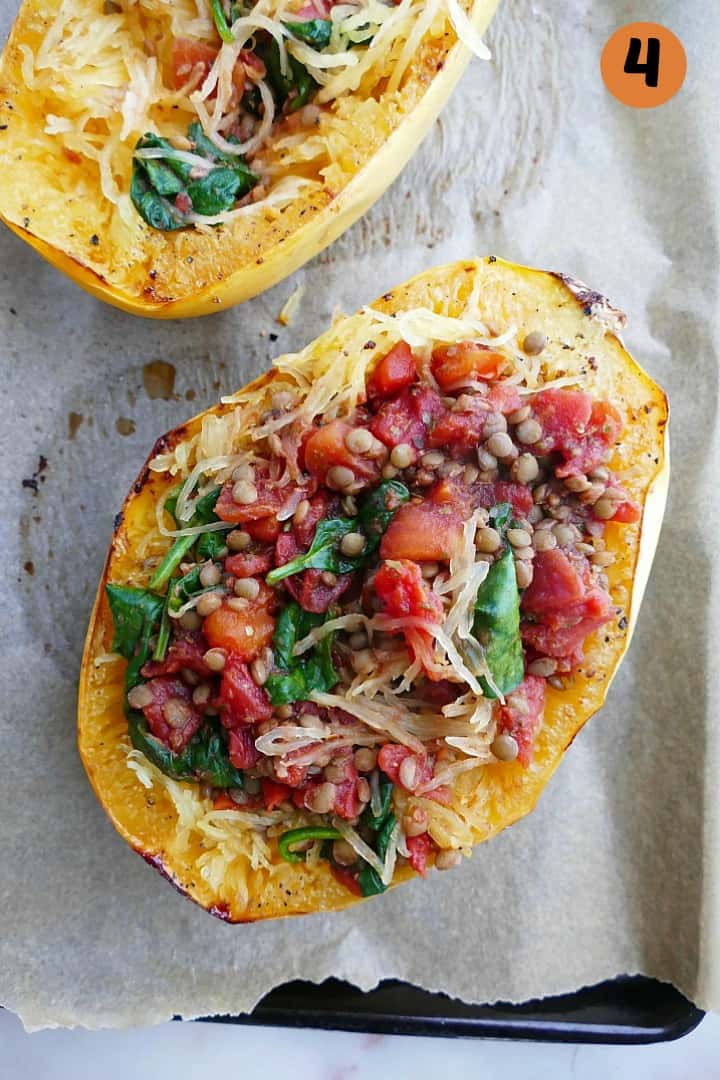 stuffed spaghetti squash with tomatoes and lentils on a lined backing sheet