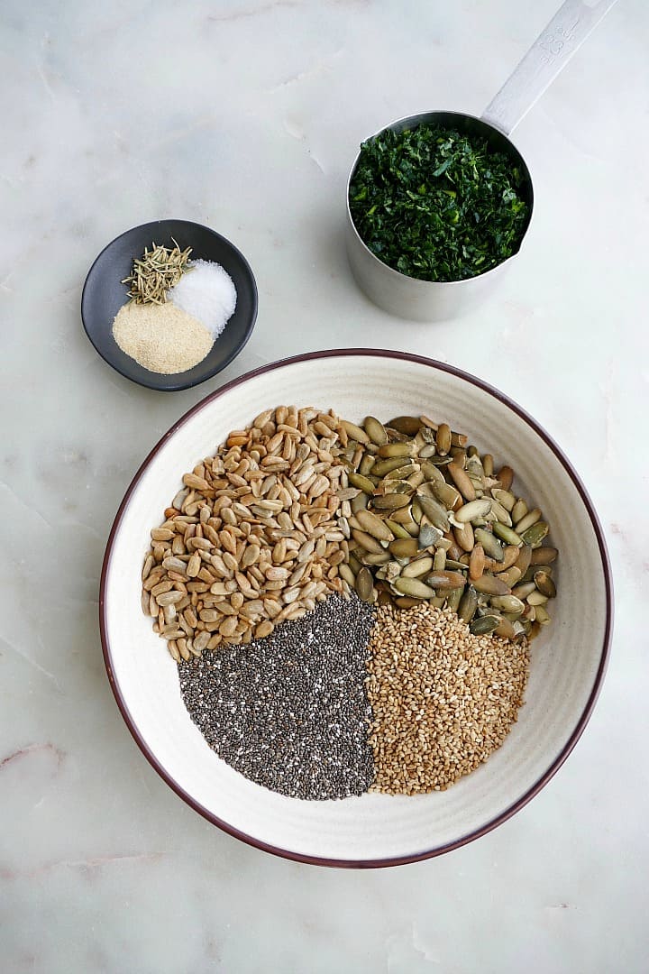 bowl with chia, pumpkin, sunflower, and sesame seeds next to a bowl with spices and kale
