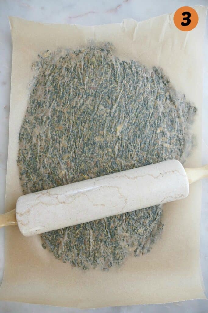a piece of parchment and a rolling pin on top of a mixture for kale crackers