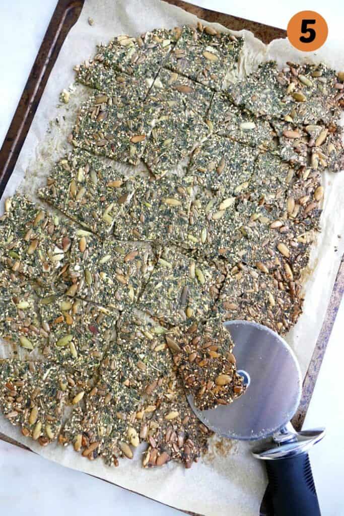 baked kale crackers on parchment on a baking sheet with a pizza cutter