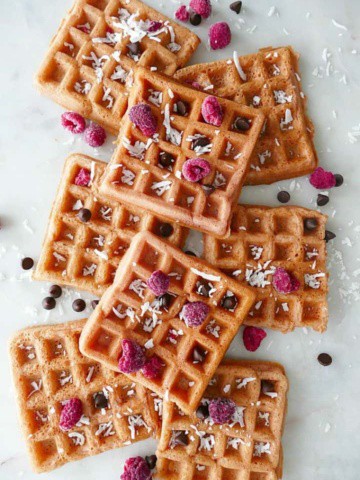 8 pink waffles on a white counter with a variety of toppings