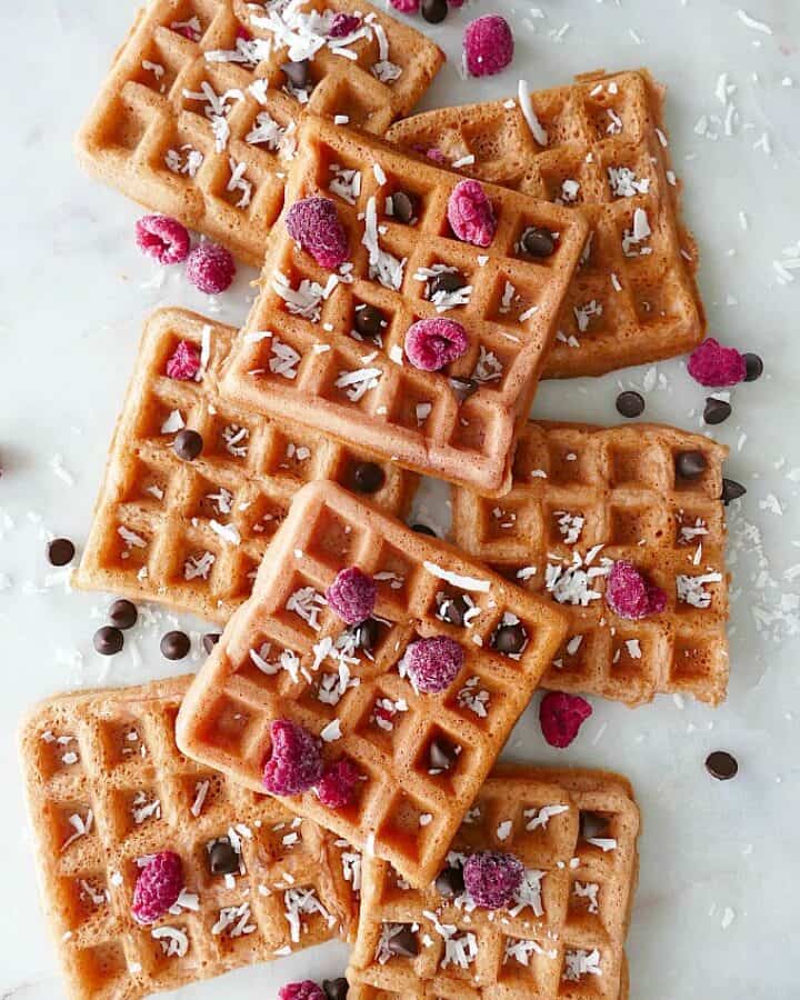8 pink waffles on a white counter with a variety of toppings