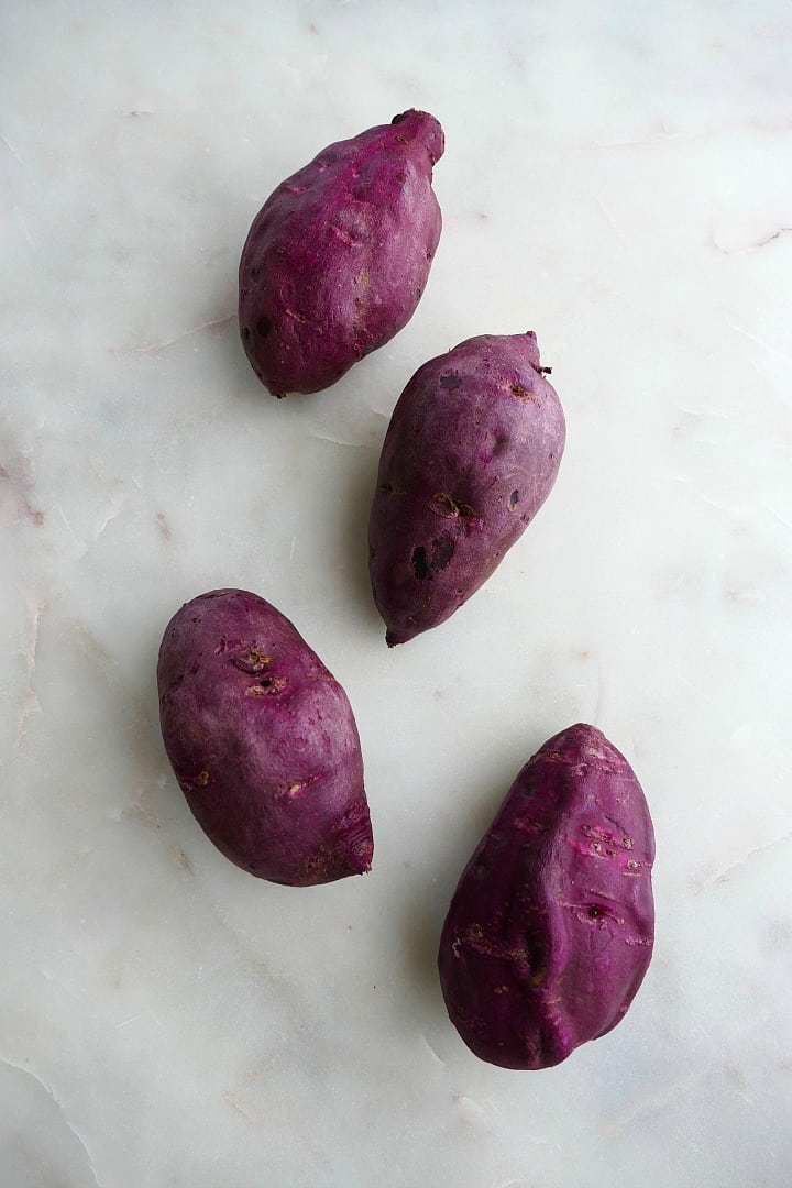 4 purple sweet potatoes next to each other on a white counter